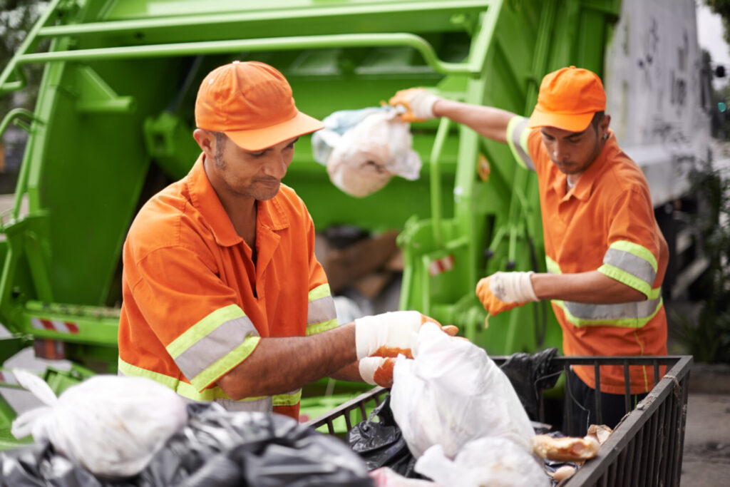 Garbage truck collecting plastic waste during city sidewalk cleaning for eco-friendly waste management.